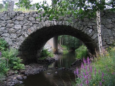 An Old Stone Bridge Over A Stream In The Woods With Wildflowers And