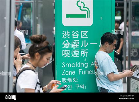 People Smoke In A Designated Smoking Area Outside Shibuya Station On