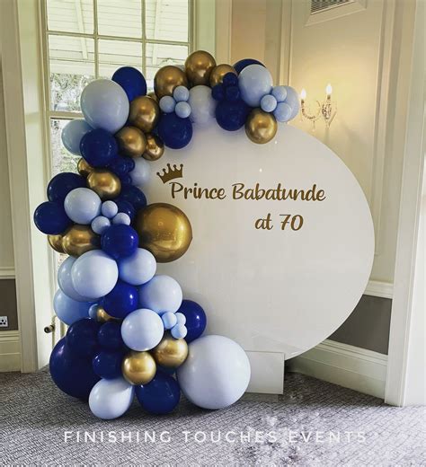 A White Sign With Blue And Gold Balloons Hanging From Its Sides In