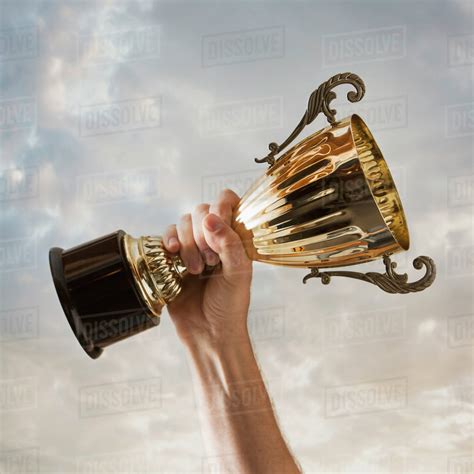 Hand Holding Trophy Against Sky Stock Photo Dissolve