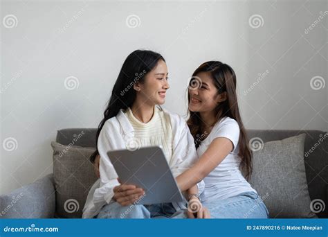 Happy Young Asian Lesbian Couple Hugging Having Fun Using Digital Tablet Relaxing On Couch At