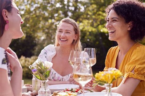 Three Female Friends Sitting Outdoors In Summer Garden At Home Eating Meal Together Stock Image