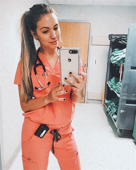 A Woman In Pink Scrubs Is Looking At Her Cell Phone