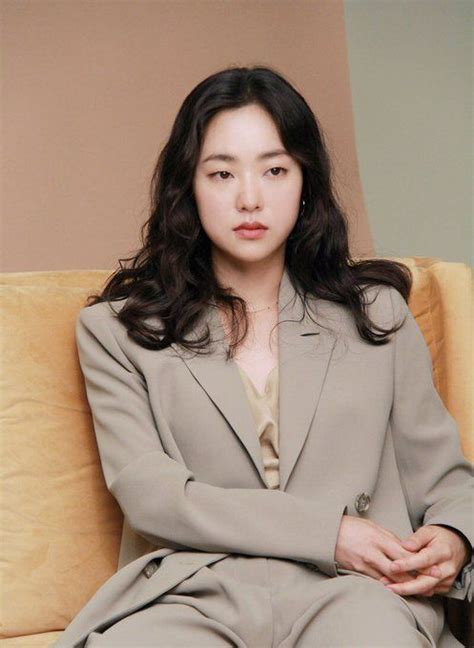 A Woman Sitting On Top Of A Couch Wearing A Gray Suit And Tan Shirt