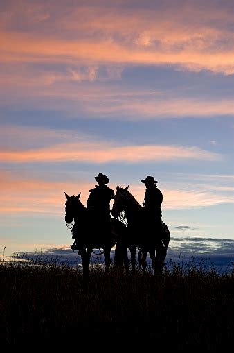 Silhouette Of Two Cowboys Riding Horses At Sunset Stock Photo