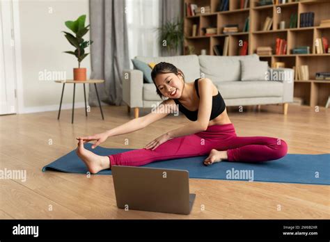 Home Training Young Japanese Lady Stretching Leg Muscles In Front Of Laptop Watching Video