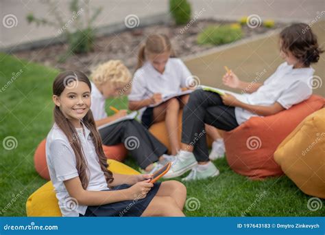 Pretty Dark Haired Schoolgirl Sitting With Classmates And Smilling