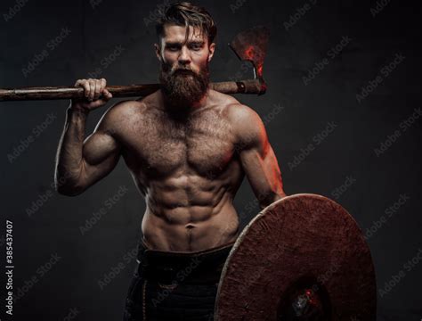 Warlike And Furious Viking With Naked Torso And Beard Staying In Dark