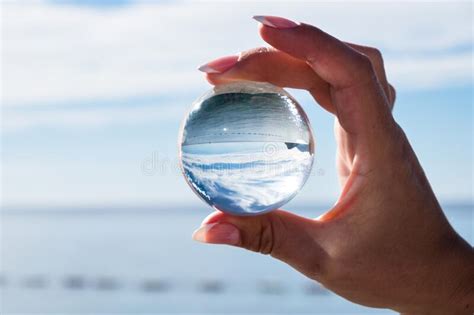 Woman Hand Holding A Crystal Ball Looking Through To The Ocean And Sky
