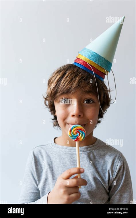 Portrait Of Little Boy With Lollipop And Four Party Hats On His Head