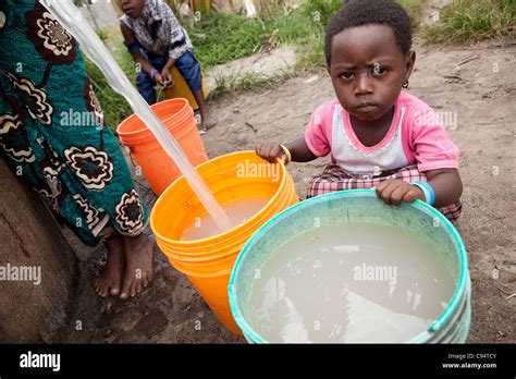 A Child Sits With Dirty Water At A Well Outside Dar Es Salaam Stock