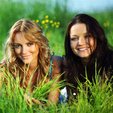 Two Young Beautiful Smiling Women Reading Book Sitting On Grass