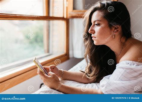 Close Up Portrait Of Young Sad Woman Lying On The Bed Looking At Her Smartphone Feels Unhappy