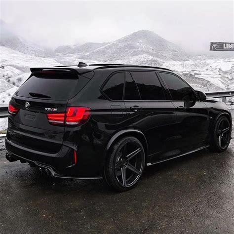 A Black Bmw Suv Parked On The Side Of A Road With Mountains In The
