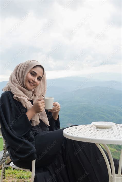 Arab Women In Hijab Holding Coffee Sitting On The Background Of Mountain And Looking At Camera