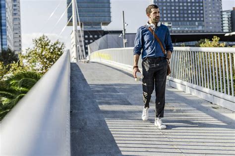 Man With Headphones And Coffee To Go Walking On A Footbridge Stock Photo