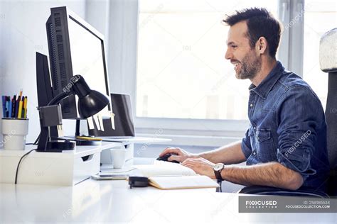 Smiling Man Working On Computer At Desk In Office — Casual Business