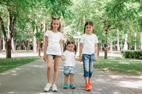 Tres Hermanas Pequeñas Con Camisetas Blancas Sentadas En El Parque Al