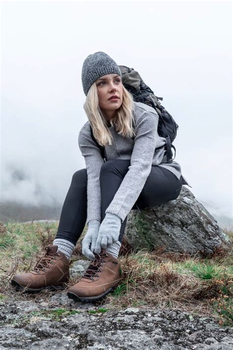 a woman sitting on top of a rock with her hands in the air while wearing hiking gear