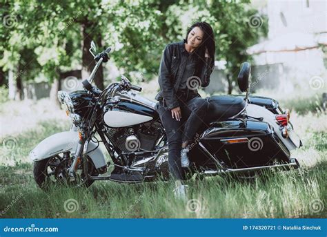 A Female Biker Is Sitting On Her Motorcycle On A Sunny Summer Day