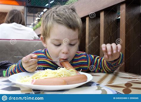 A Boy Child Eats Sausage Food At A Table In A Cafe Stock Photo Image