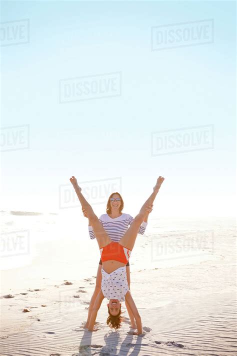 Woman Helping Friend Do Handstand On Beach Stock Photo Dissolve