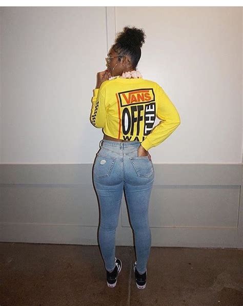 A Woman In Yellow Shirt And Jeans Standing Next To Wall With Her Hands