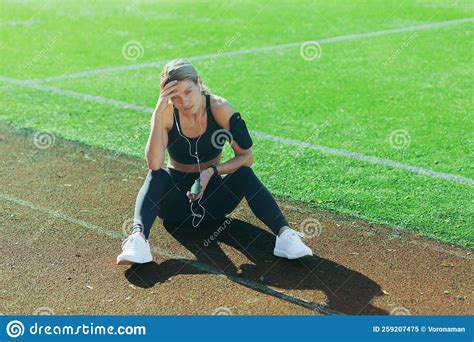tired sportswoman sitting on treadmill blonde resting after jogging woman listening to music