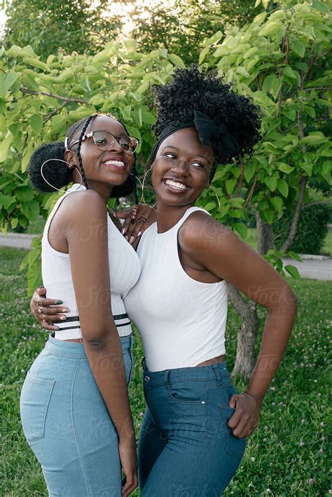 Two African Girls In Jeans And White Tops Are Hugging In The Park By
