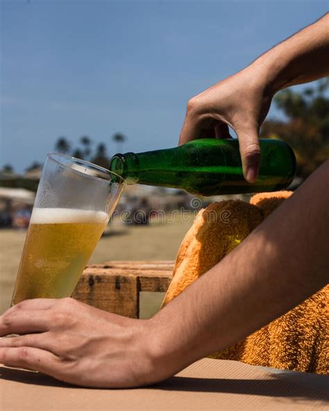 Closeup Shot Of Hands Pouring Cold Beer Into A Glass At A Beach Stock