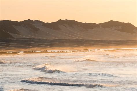 Waving Sea Surrounded By Sandy Dunes And Mountains During Sundown