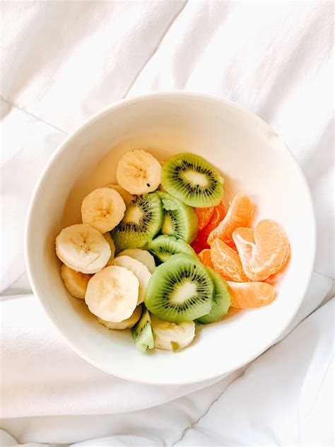 A White Bowl Filled With Sliced Fruit On Top Of A Bed