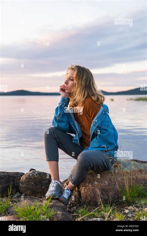 Finland Lapland Young Woman Sitting On A Rock At The Lakeside Stock