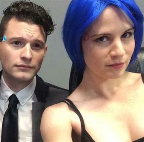 A Woman With Blue Hair Standing Next To A Man In A Black Suit And Tie