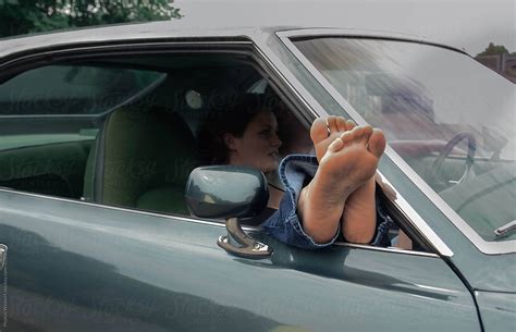 Young Woman In Passenger Seat Of Parked Car With Her Feet Sticking Out Of The Window Del