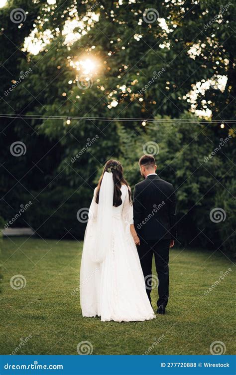 Newlywed Couple Walking Hand In Hand Through A Lush Field At Sunset