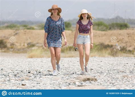 Two Beautiful Girls In Straw Hat Walk Along A Beach In