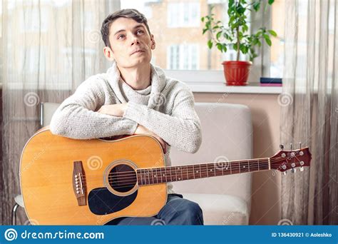 Young Attractive Male Musician Sitting On A Chair Holding An Acoustic