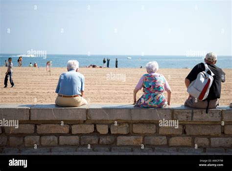 A Rear View Of Three Old People Sitting On Wall Overlooking A Beach