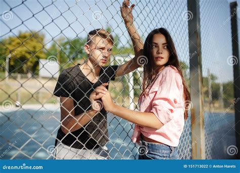 Young Beautiful Girl And Boy Standing Between Mesh Fence On Basketball