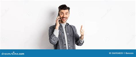 Excited Young Man Talking On Phone And Showing Thumbs Up Smiling Satisfied Standing Against