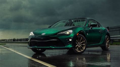 A Green Sports Car Is Parked On The Side Of The Road With Dark Clouds In The Background