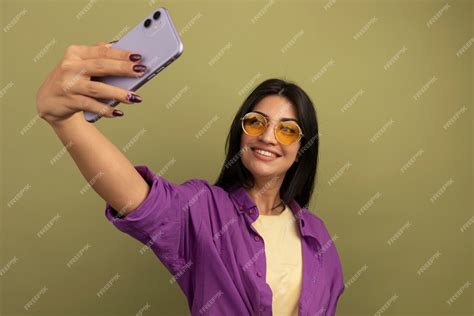 Free Photo Smiling Pretty Brunette Woman In Sun Glasses Holds And Looks At Phone Taking Selfie