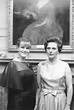 two women standing next to each other in front of a painting