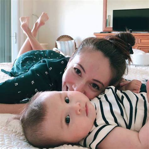 A Woman Laying On Top Of A Bed Next To A Baby In Her Lap And Smiling At