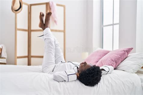 Young African American Woman Lying On Bed With Legs Raised Up At