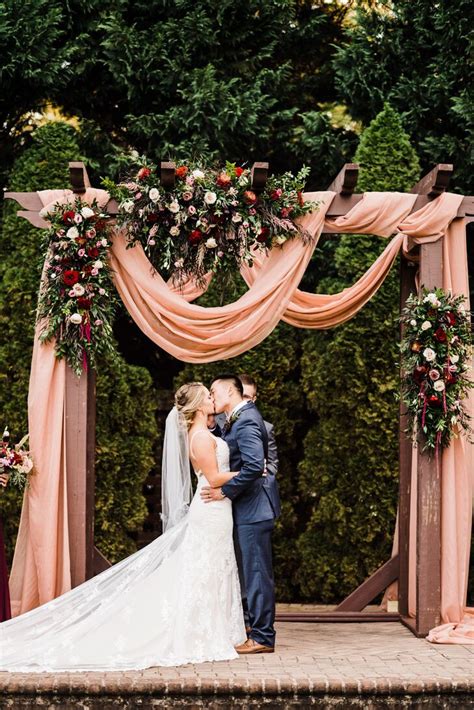 couple under wedding arch with pink draping roses and greenery