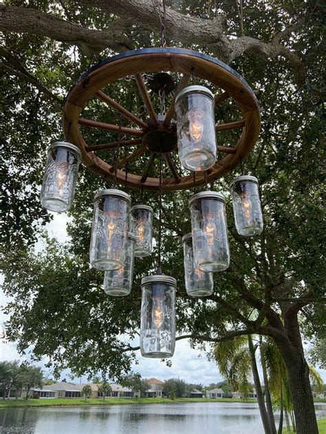 Mason Jar Chandelier Hanging From A Tree Over A Lake With Lights In It