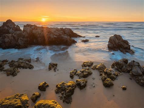 Premium Ai Image A Sunset Over The Ocean With Rocks And The Sun