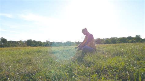 Young Man Sitting At Green Grass In The Meadow And Doing Yoga Exercise